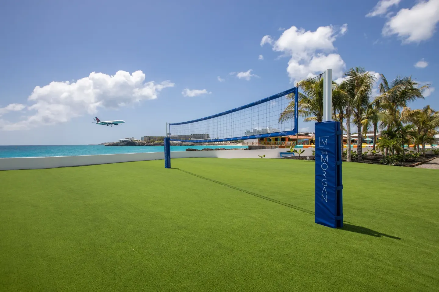 Oceanfront volleyball court at The Morgan Resort Spa Village with a plane landing nearby.