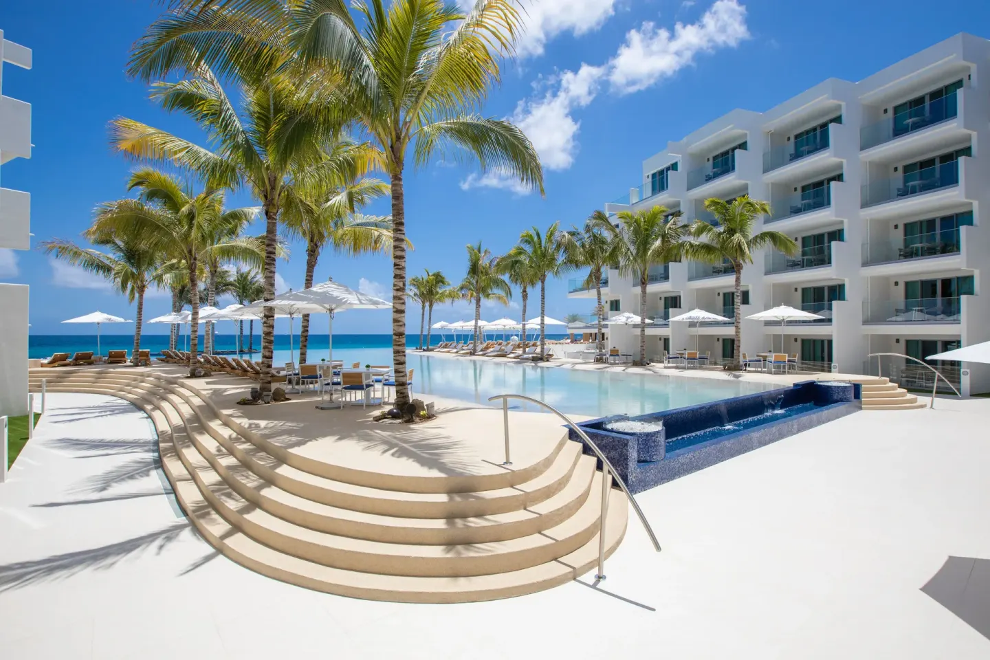 Palm-lined pool deck and ocean beyond the buildings at The Morgan Resort Spa Village.