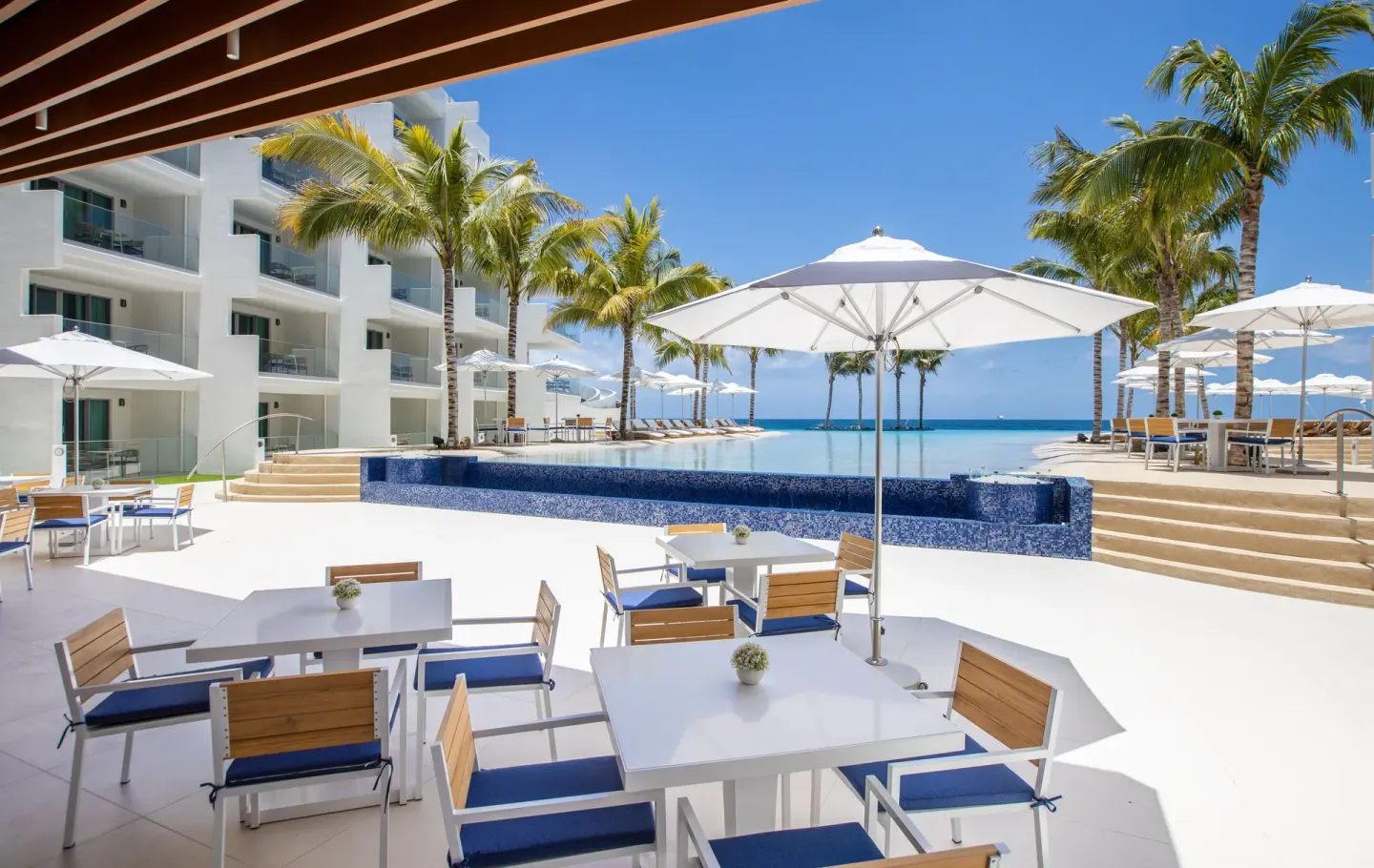 Poolside tables at The Morgan Resort Spa Village beside umbrellas, palms, and the infinity pool.