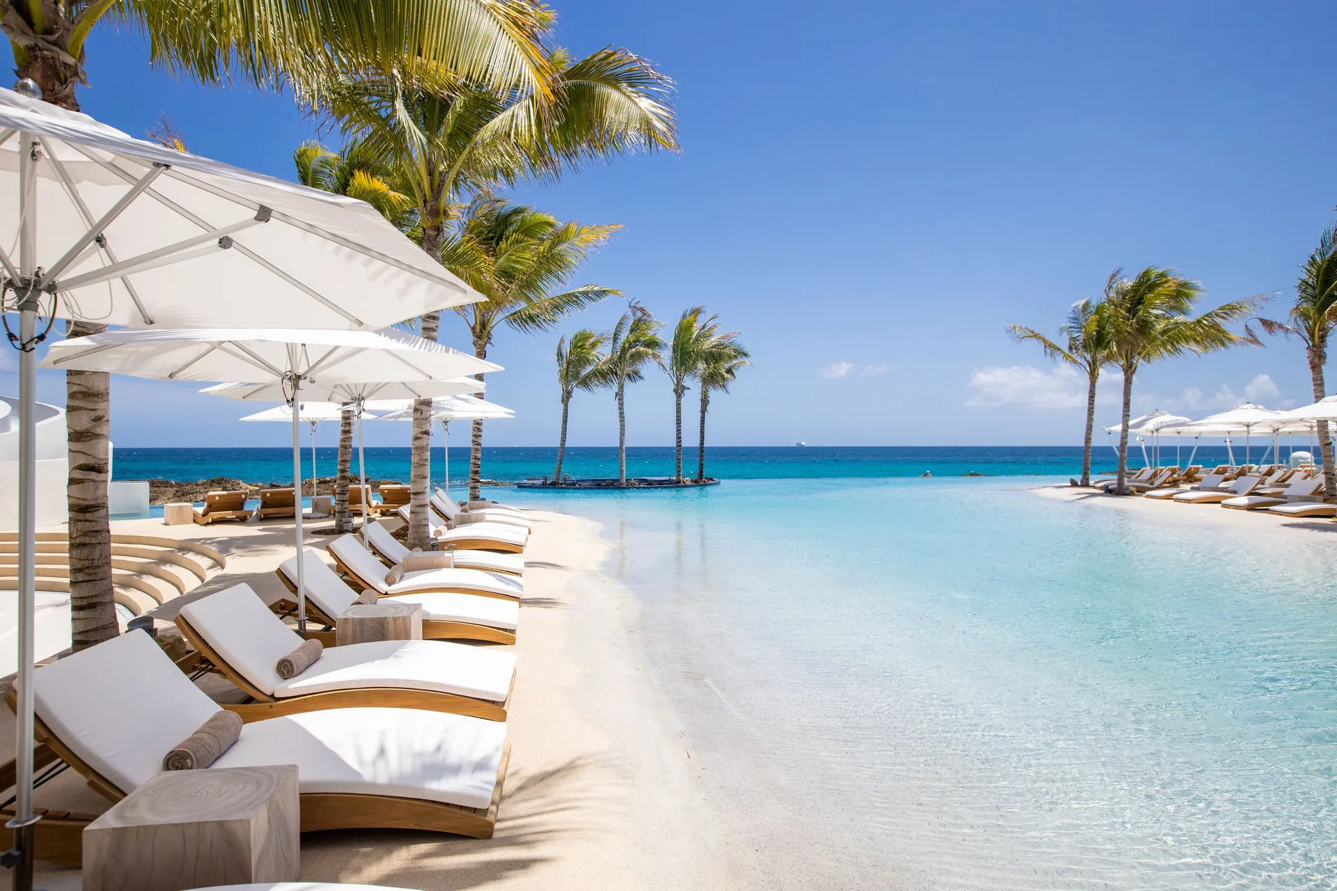 Curved loungers and white umbrellas border the turquoise pool at The Morgan Resort Spa Village.