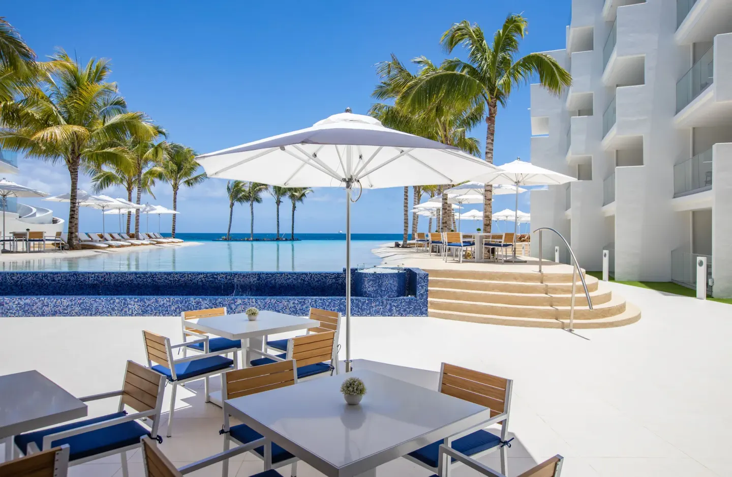 Umbrella-shaded poolside seating at The Morgan Resort Spa Village near steps and palms.