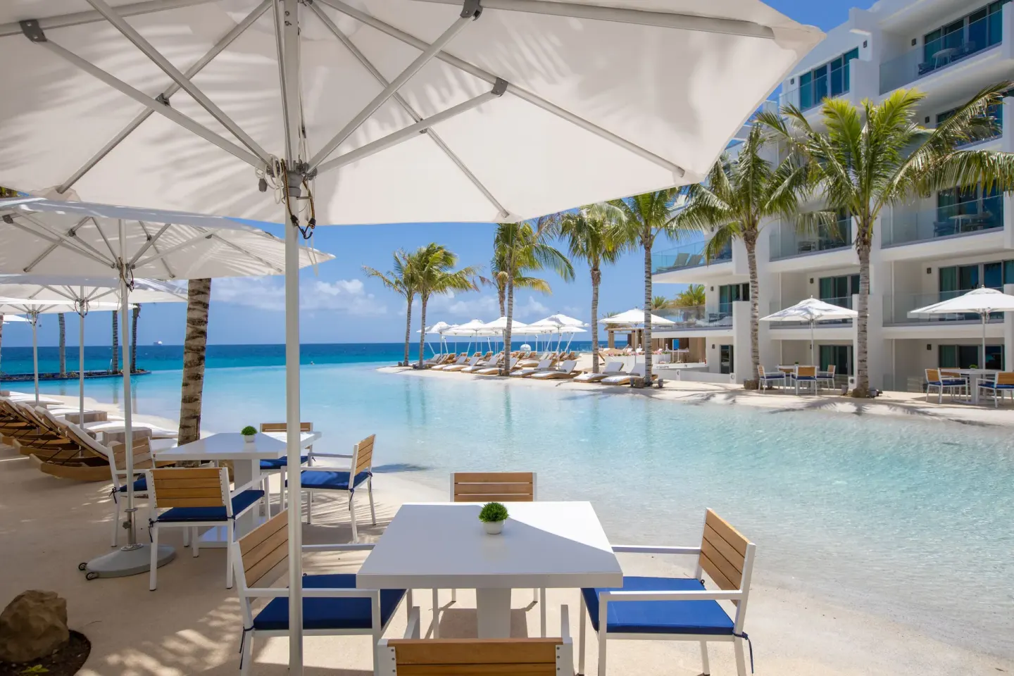 Umbrella-shaded tables beside the beachfront pool at The Morgan Resort Spa Village.