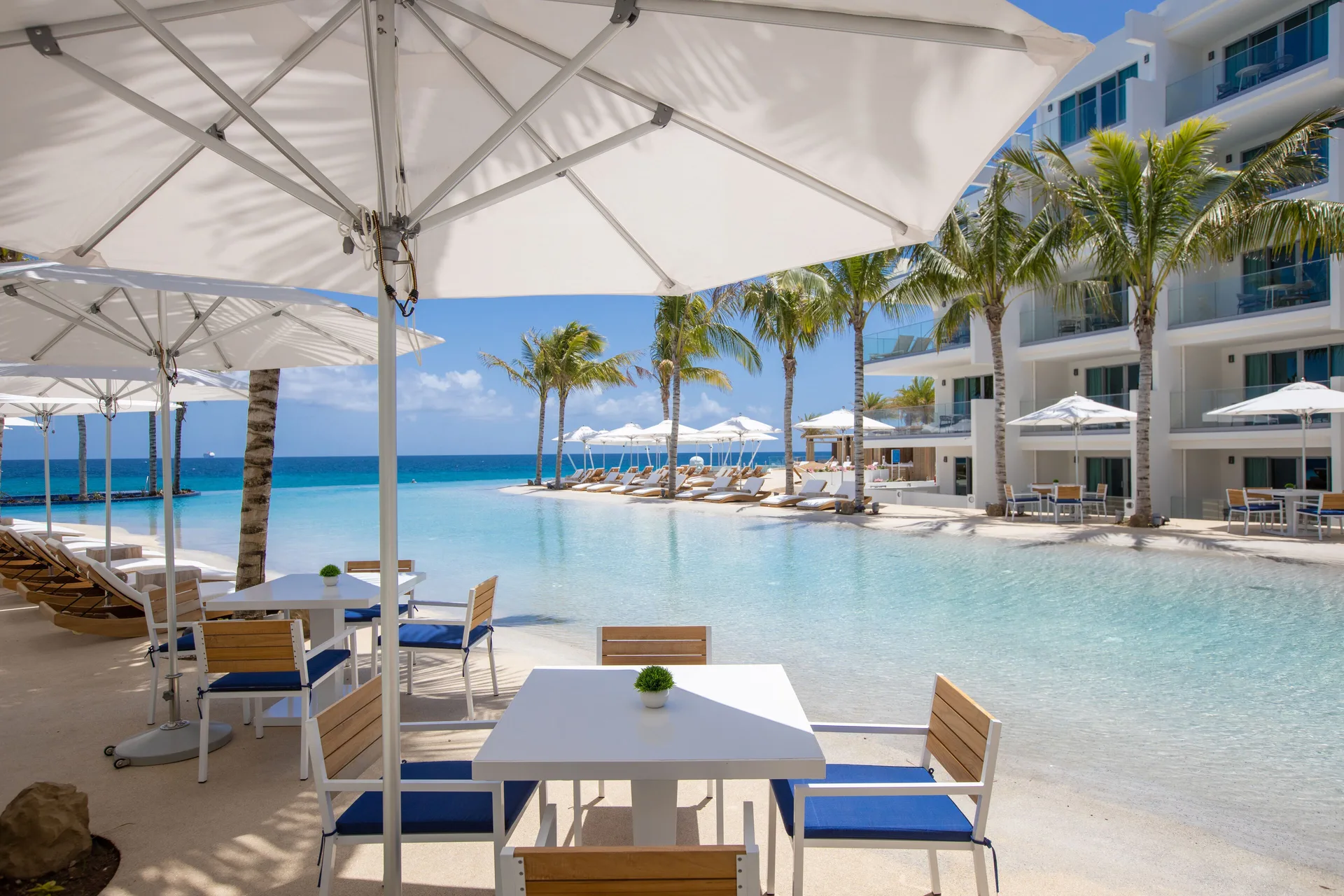 Umbrella-shaded tables beside the beachfront pool at The Morgan Resort Spa Village.