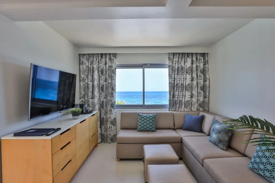 Junior Oceanfront Suite lounge with sofa, TV, and ocean window at The Morgan Resort Spa Village.