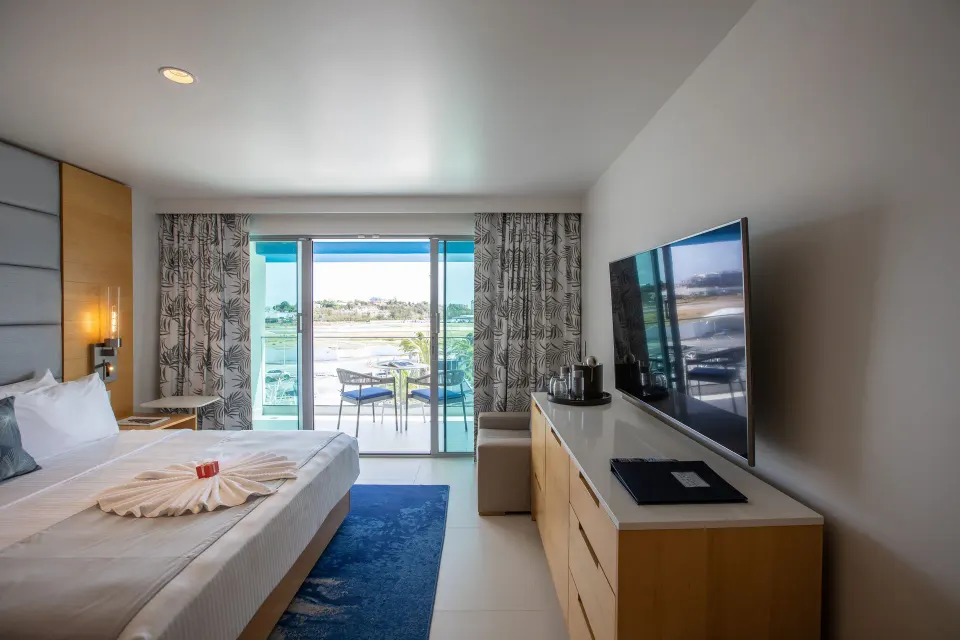 Runway View Guestroom king bed and TV facing balcony at The Morgan Resort Spa Village.