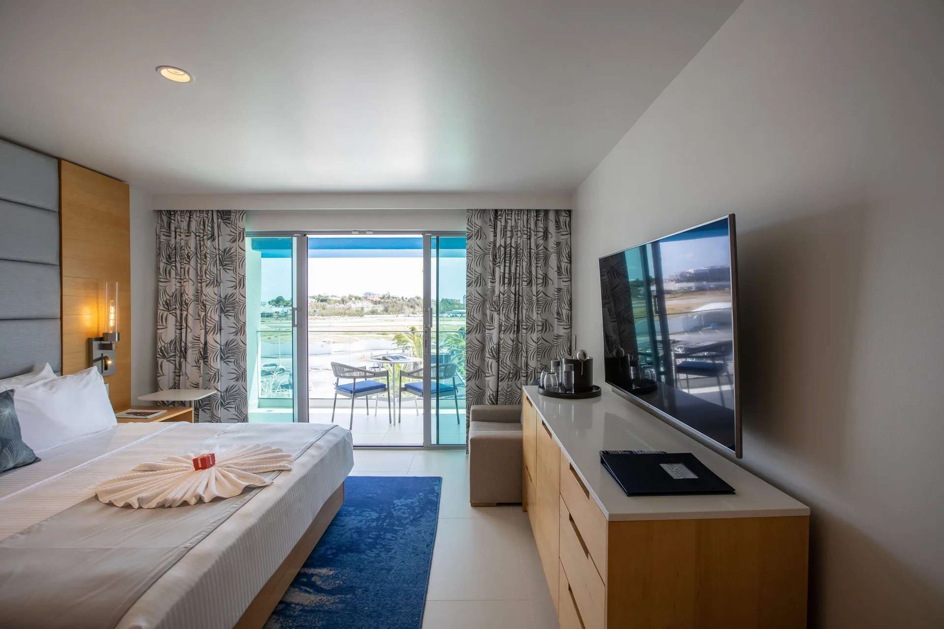 Runway View Guestroom king bed and TV facing balcony at The Morgan Resort Spa Village.