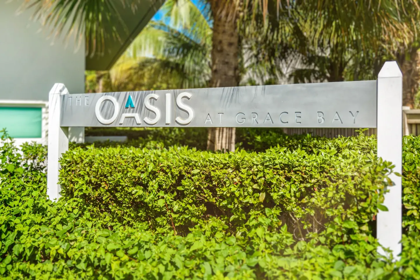 Entrance sign for The Oasis at Grace Bay behind green hedges and palms.