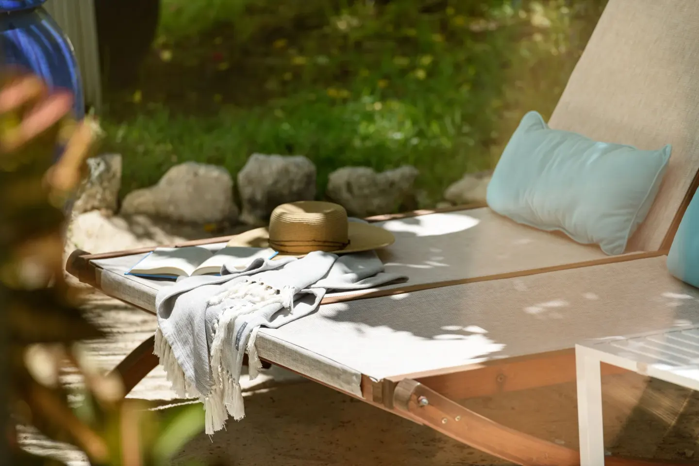 A cushioned outdoor chaise with a hat and book in the gardens at The Oasis at Grace Bay.