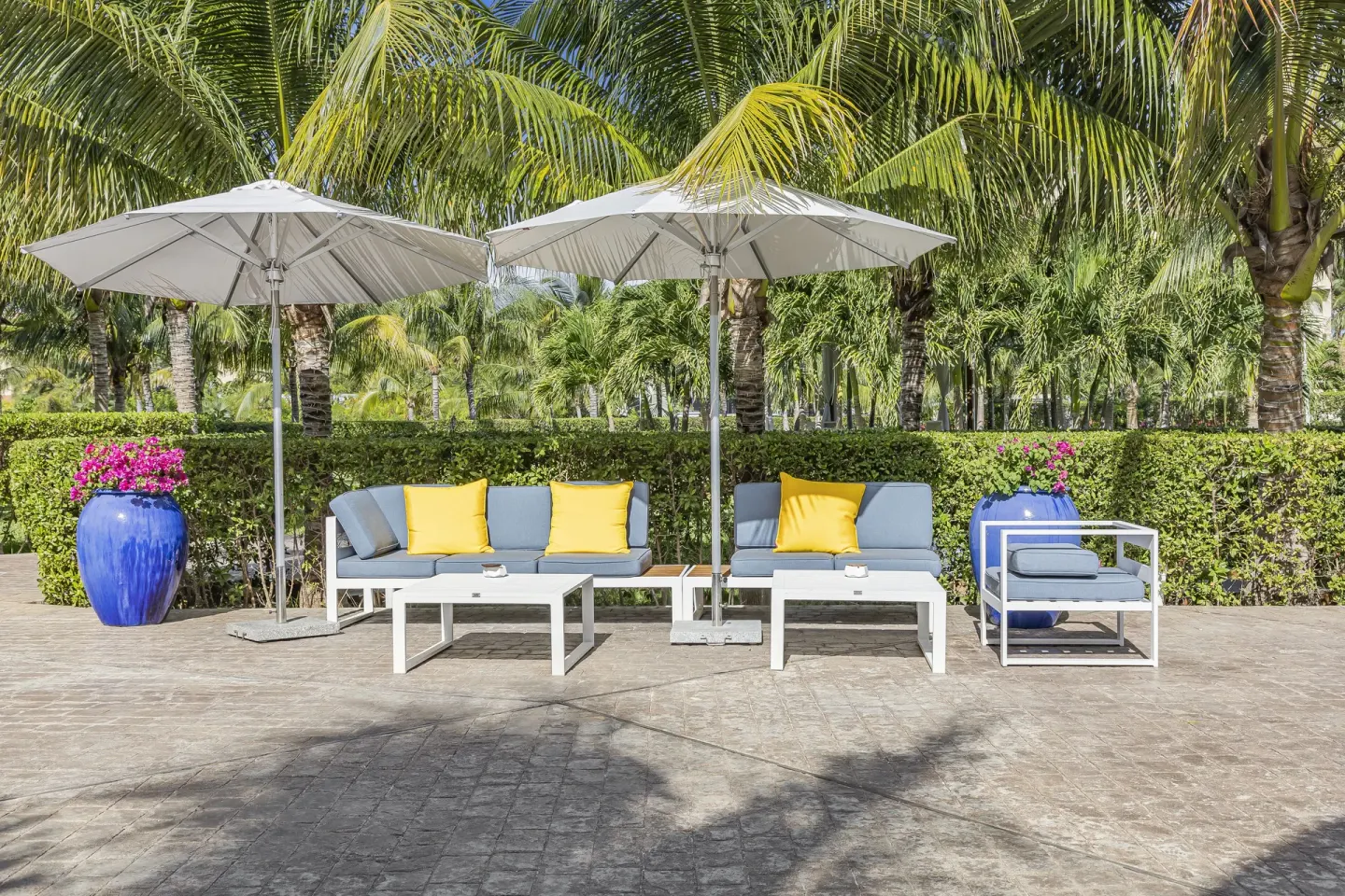 Outdoor sofas with yellow pillows and umbrellas by palms at The Oasis at Grace Bay.
