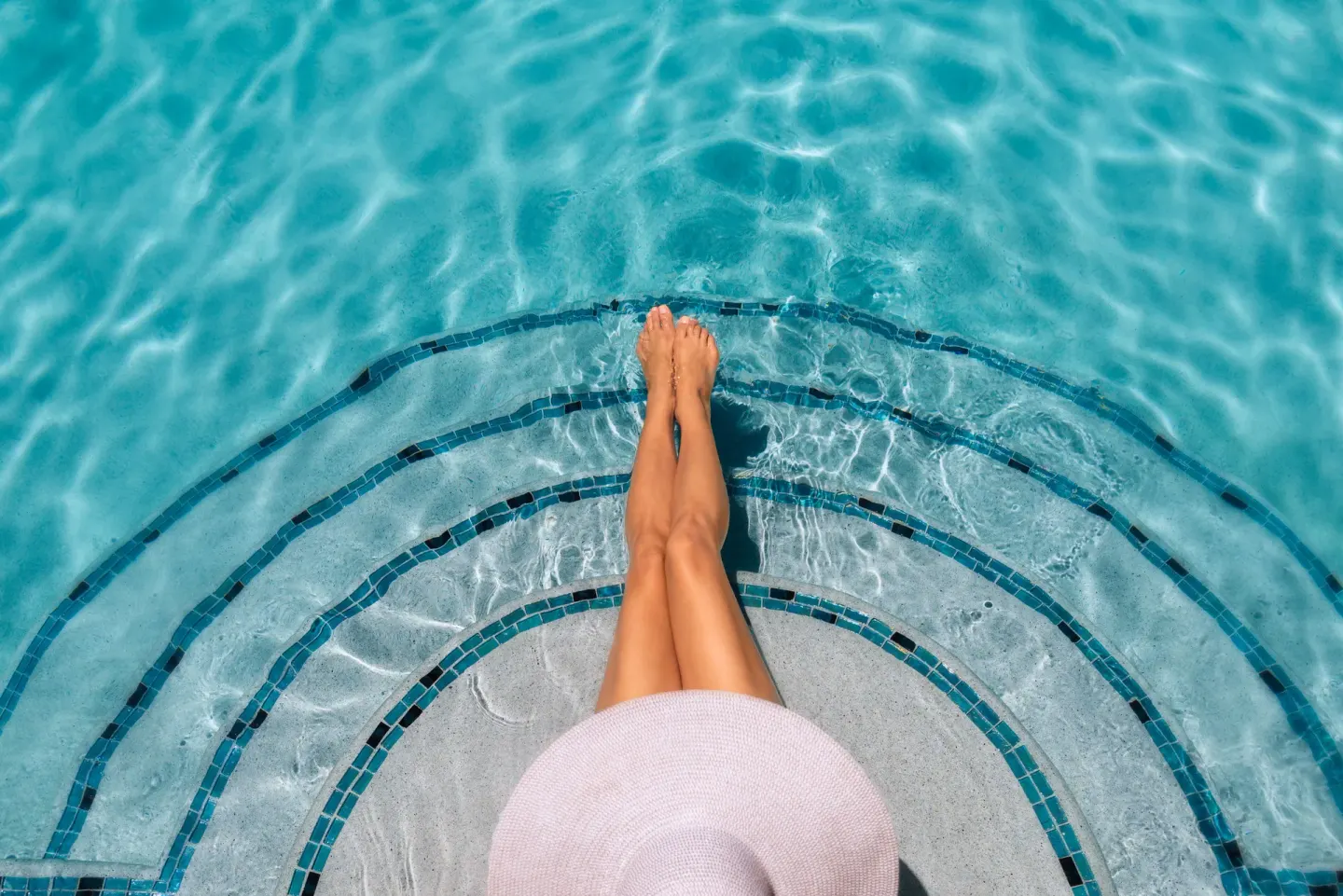 Guest's legs over curved pool steps in clear blue water at The Oasis at Grace Bay.