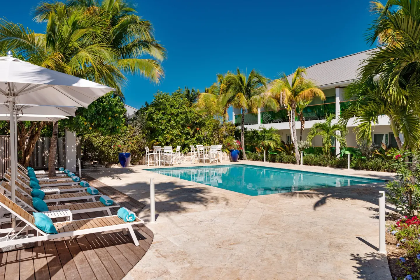 Resort pool with loungers, umbrellas, and palms at The Oasis at Grace Bay.