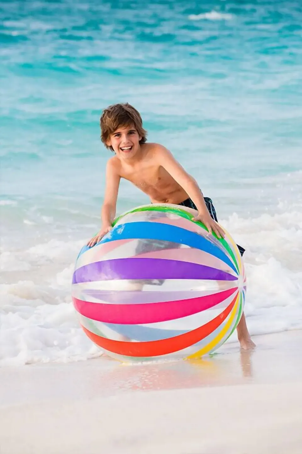 A child holds a large striped beach ball at the waterline at The Palms Turks and Caicos.