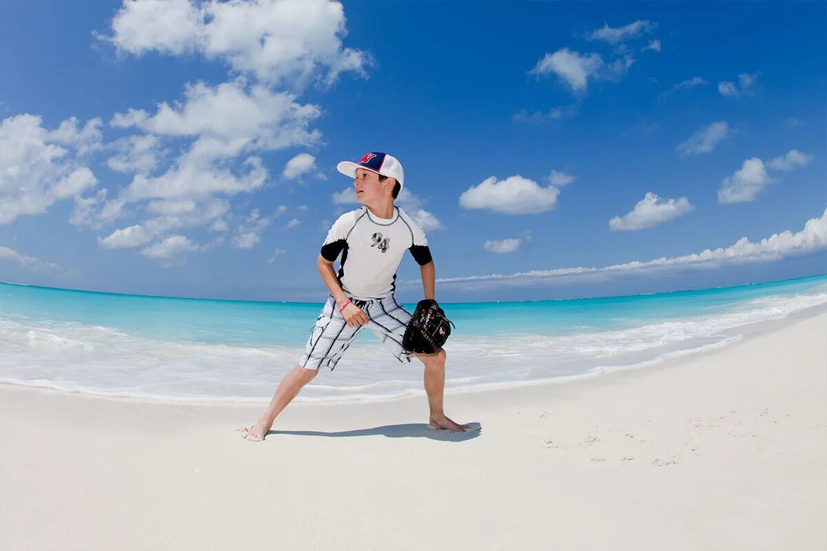 A child with a baseball glove stands on the white sand beach at The Palms Turks and Caicos.