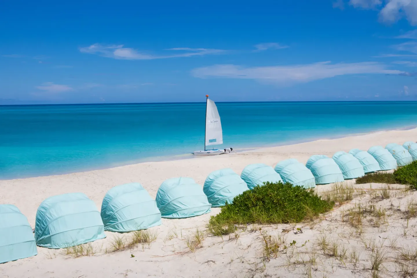 Beach cabanas and a small sailboat on the sand at The Palms Turks and Caicos.