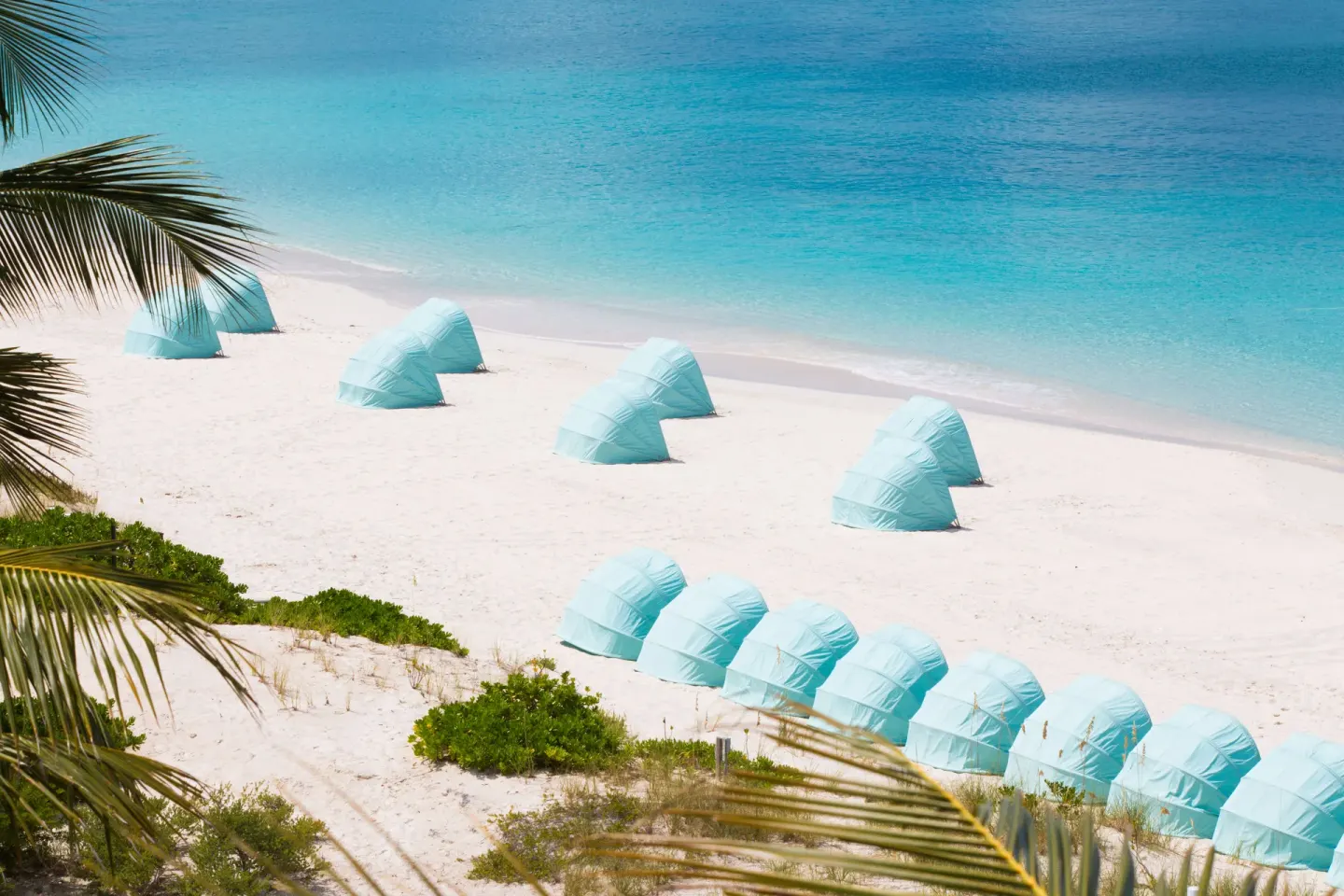 Aerial view of blue beach cabanas and clear shoreline at The Palms Turks and Caicos.