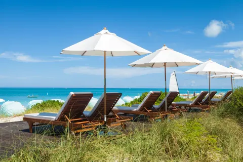 Wood loungers and white umbrellas overlooking the beach at The Palms Turks and Caicos.
