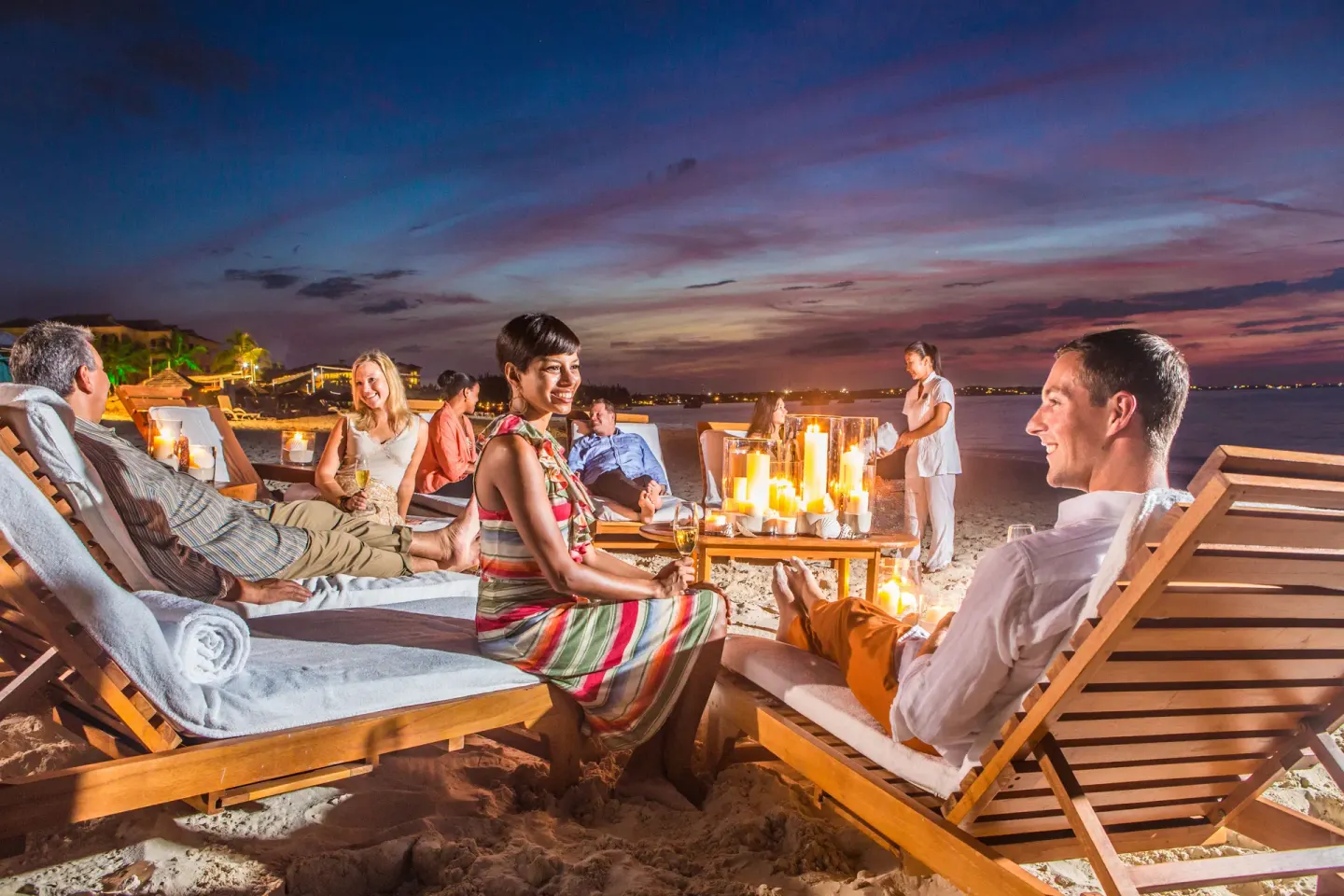 Guests relaxing on candlelit beach loungers at dusk at The Palms Turks and Caicos.