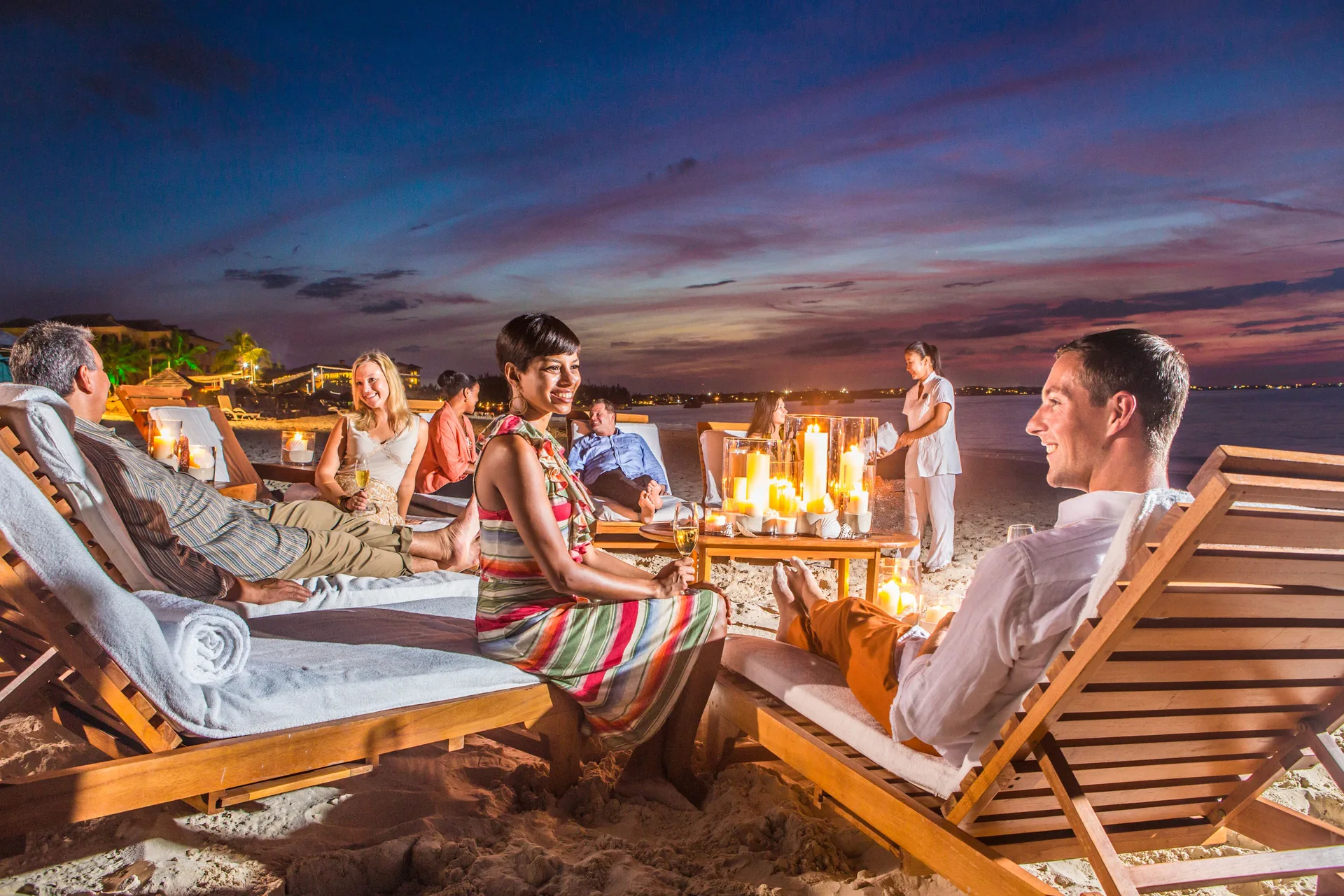 Guests relaxing on candlelit beach loungers at dusk at The Palms Turks and Caicos.