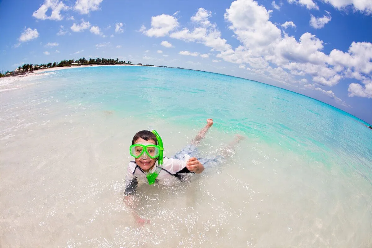 A child wearing a green snorkel mask plays in shallow water at The Palms Turks and Caicos.