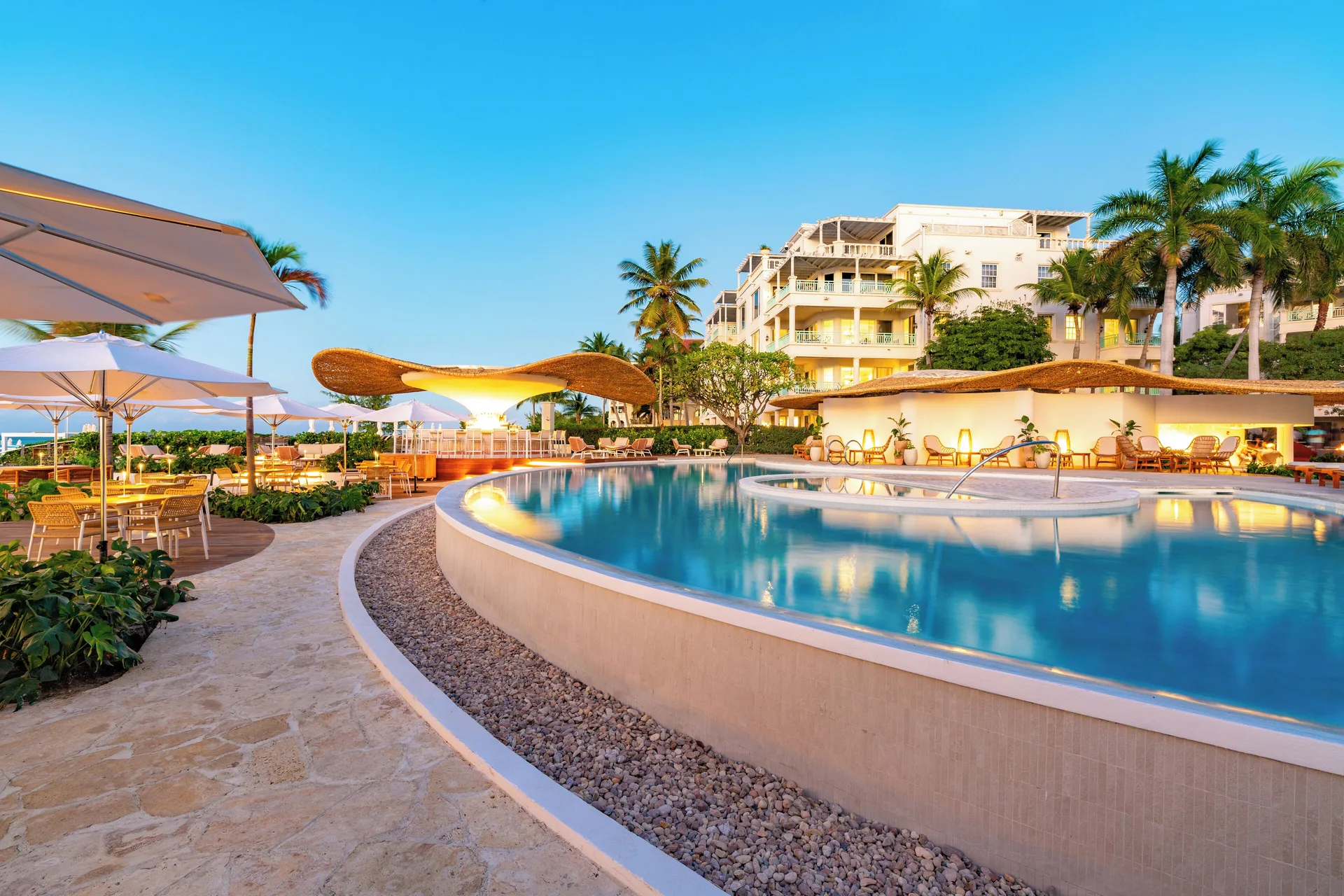 Curved resort pool with umbrellas, palms and buildings at The Palms Turks and Caicos.