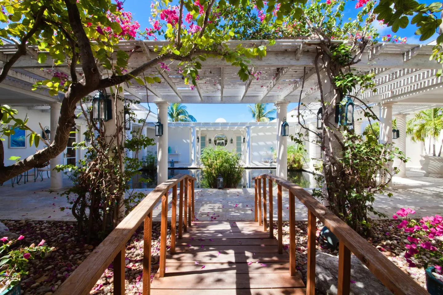 Garden walkway with a wooden bridge and flowering pergola at The Palms Turks and Caicos.