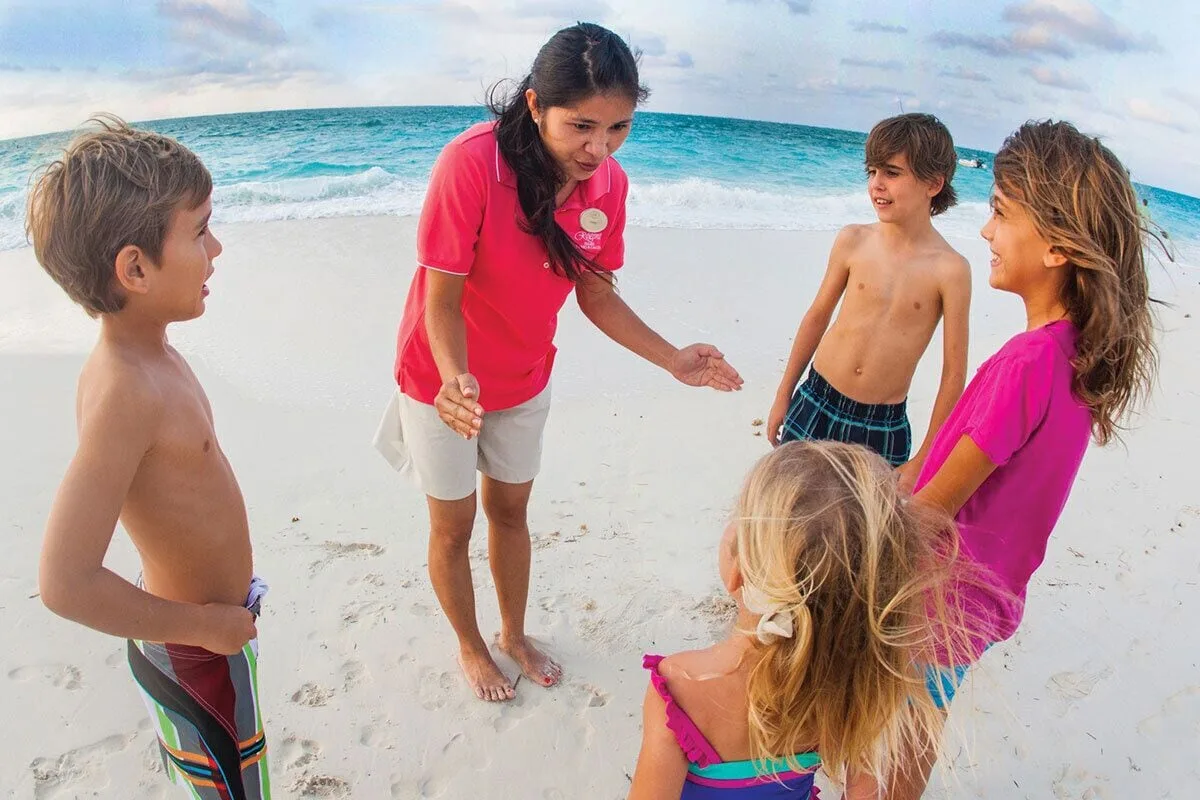 A resort staff member speaks with children on the beach at The Palms Turks and Caicos.
