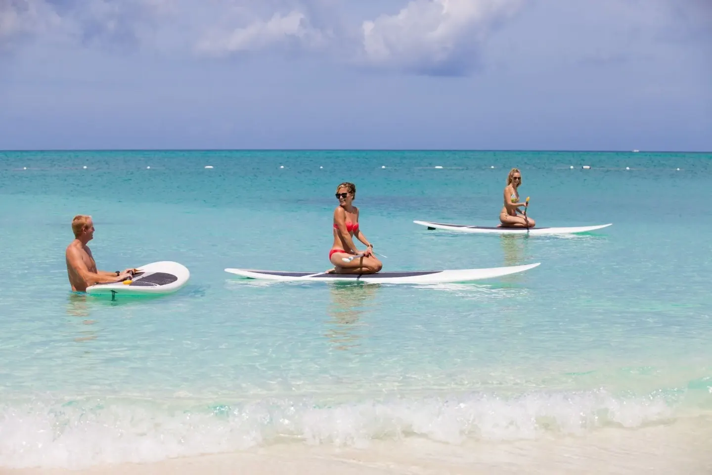 Guests sit on paddleboards in shallow ocean water at The Palms Turks and Caicos.