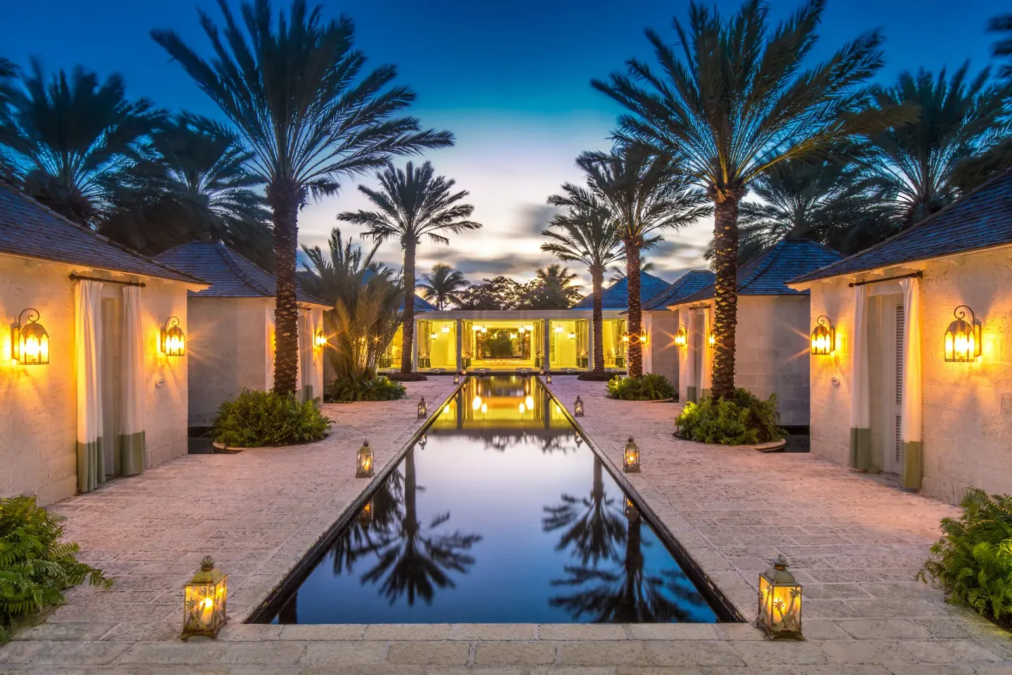 Lantern-lit reflecting pool between palms and pavilions at dusk at The Palms Turks and Caicos.
