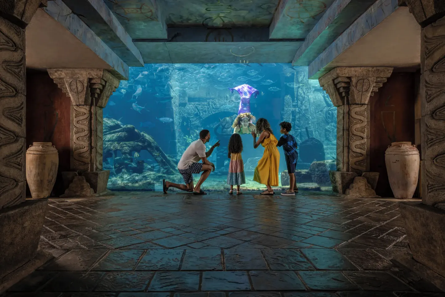 A family viewing a large aquarium window with a mermaid performer at The Reef at Atlantis.