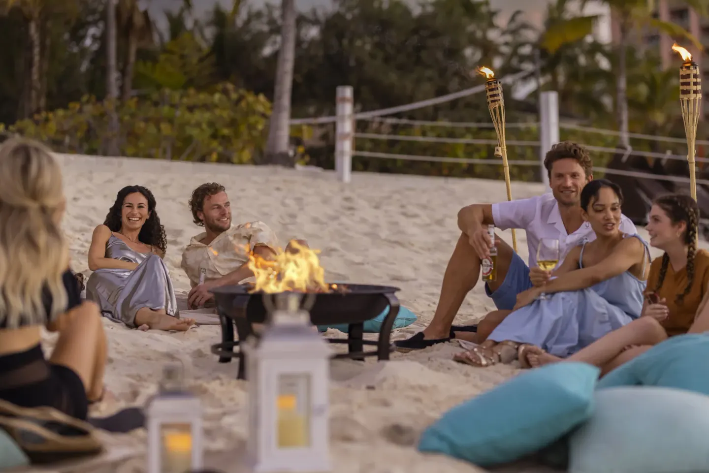 Guests sit around a beach fire pit with tiki torches at The Reef at Atlantis.