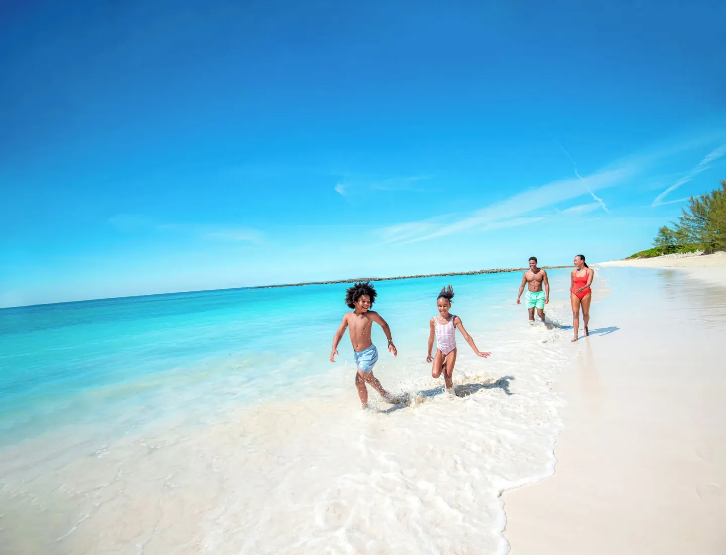 Family runs along a white-sand beach and turquoise water at The Reef at Atlantis.