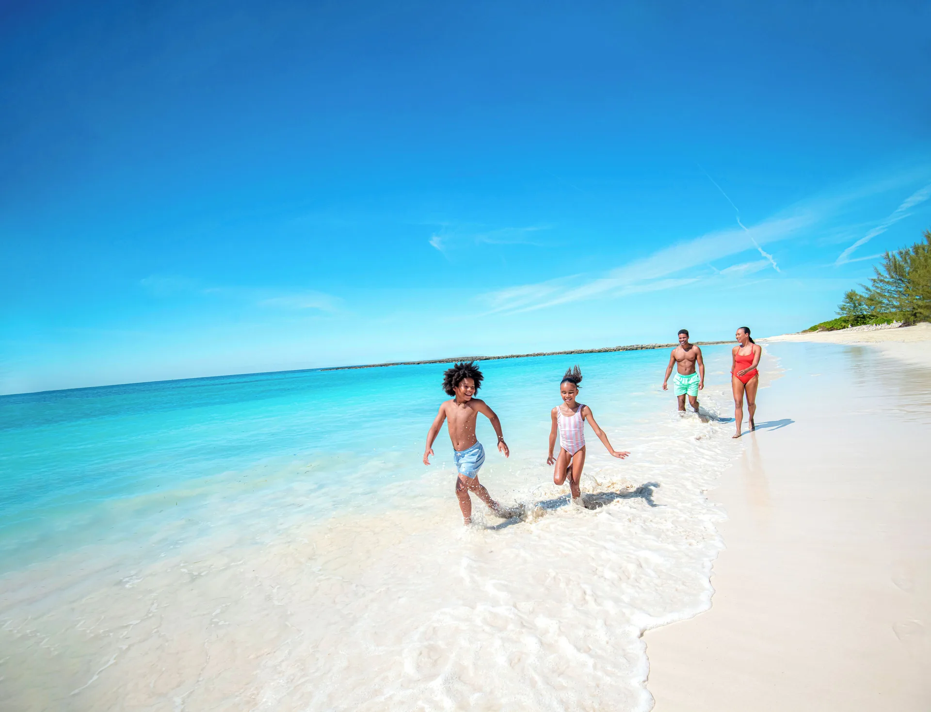 Family runs along a white-sand beach and turquoise water at The Reef at Atlantis.