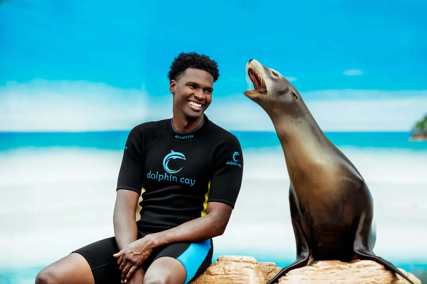 Trainer sitting beside a sea lion in a marine encounter at The Reef at Atlantis.