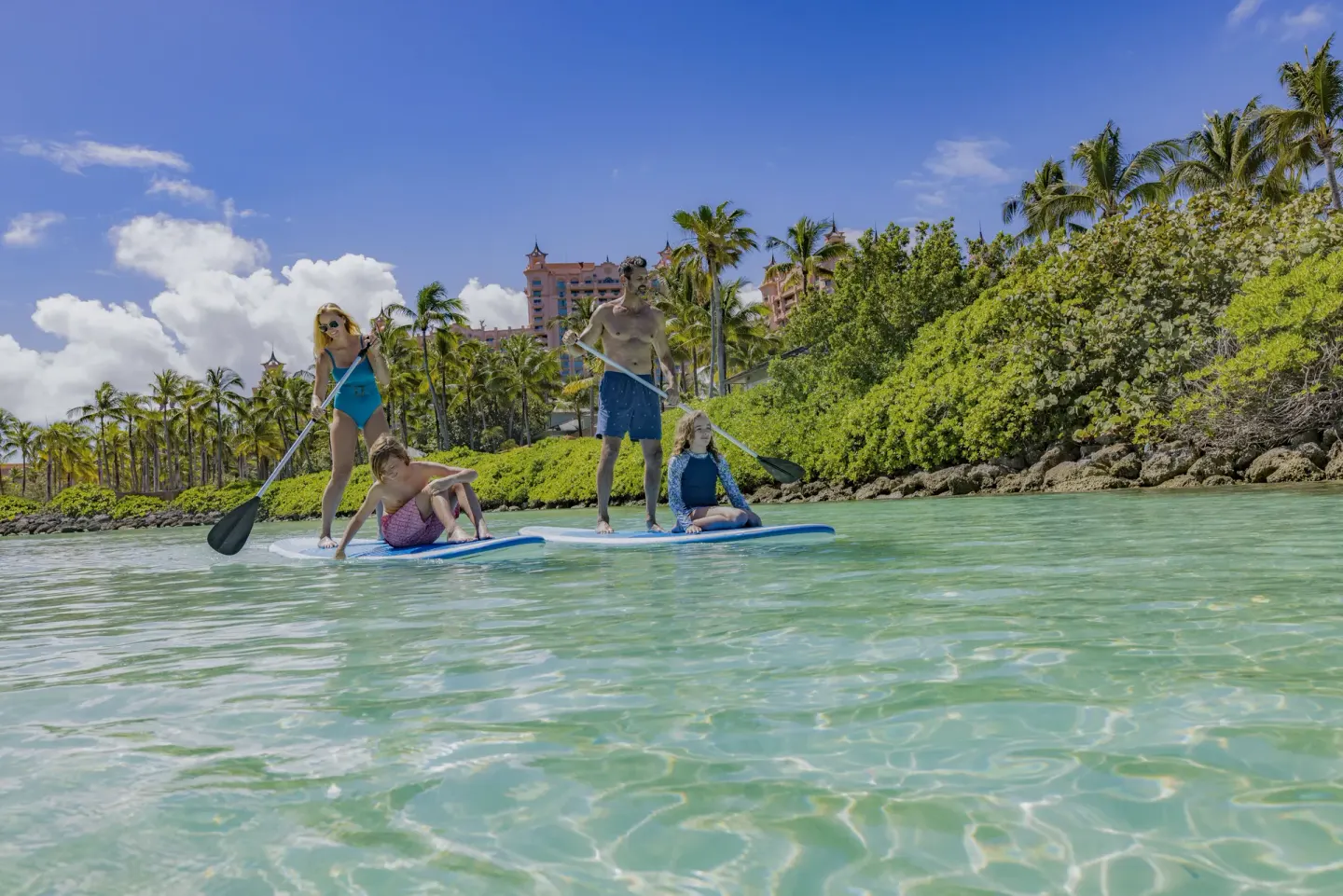 Guests paddleboard in clear turquoise water by The Reef at Atlantis.