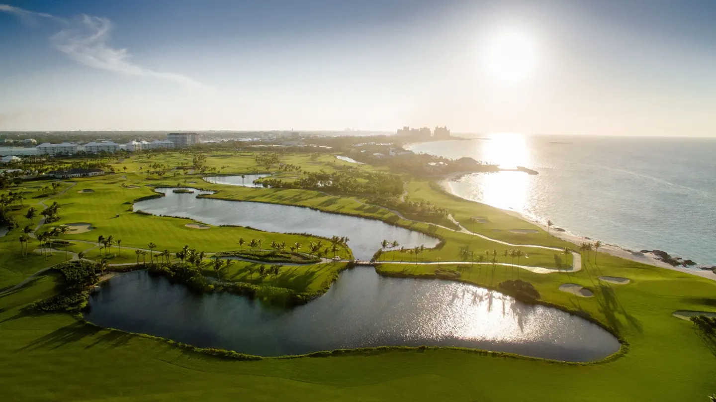 Sunlit aerial view of golf greens, ponds, and ocean near The Reef at Atlantis.