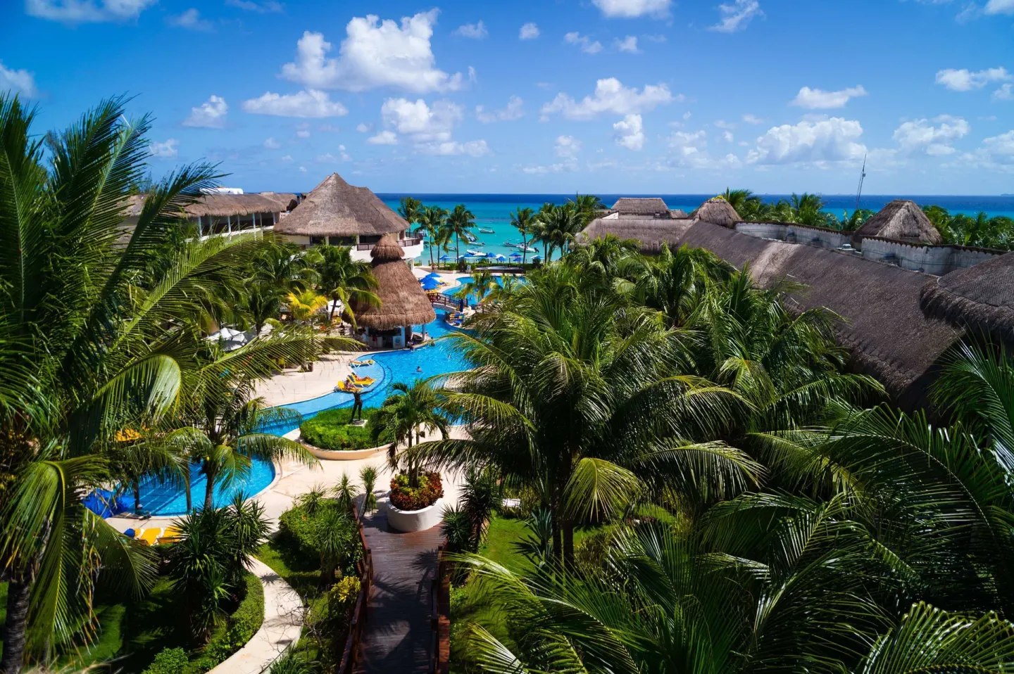 Aerial view of pools, palms, thatched roofs, and the sea at The Reef Coco Beach Resort & Spa.