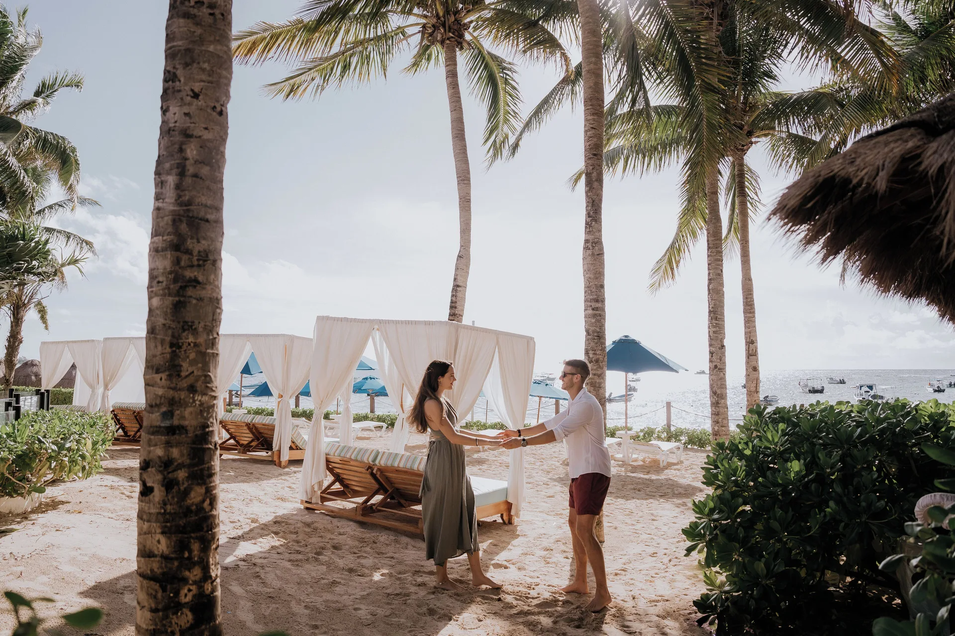 Couple standing by curtained beach daybeds at The Reef Coco Beach Resort & Spa.