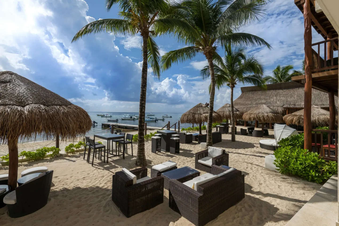 Beach lounge seating under palms and thatched shade at The Reef Coco Beach Resort & Spa.