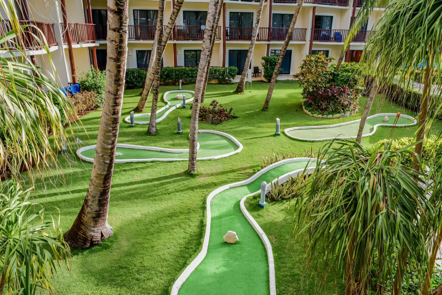 Mini golf course among palms and guestroom buildings at The Reef Coco Beach Resort & Spa.