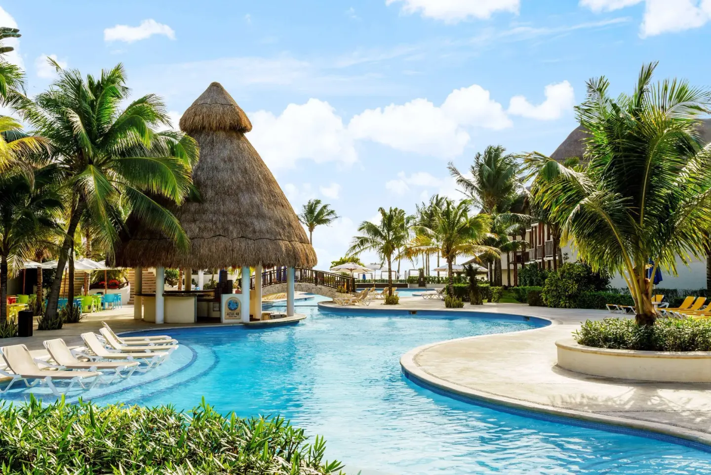 Pool with thatched swim-up bar, loungers, and palms at The Reef Coco Beach Resort & Spa.