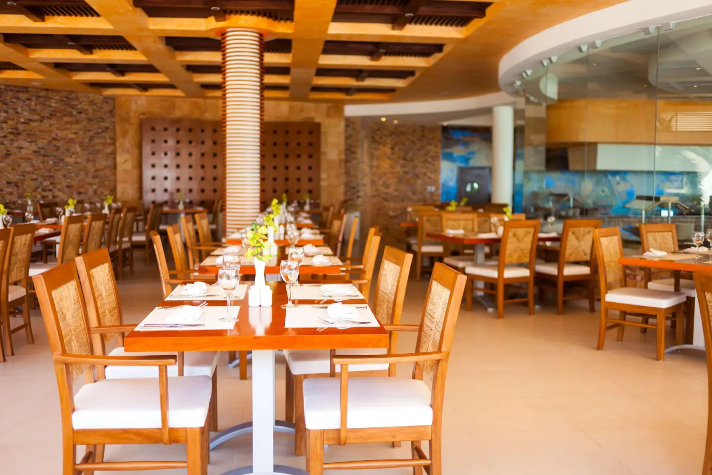 Set dining tables in a warm restaurant at The Reef Coco Beach Resort & Spa.