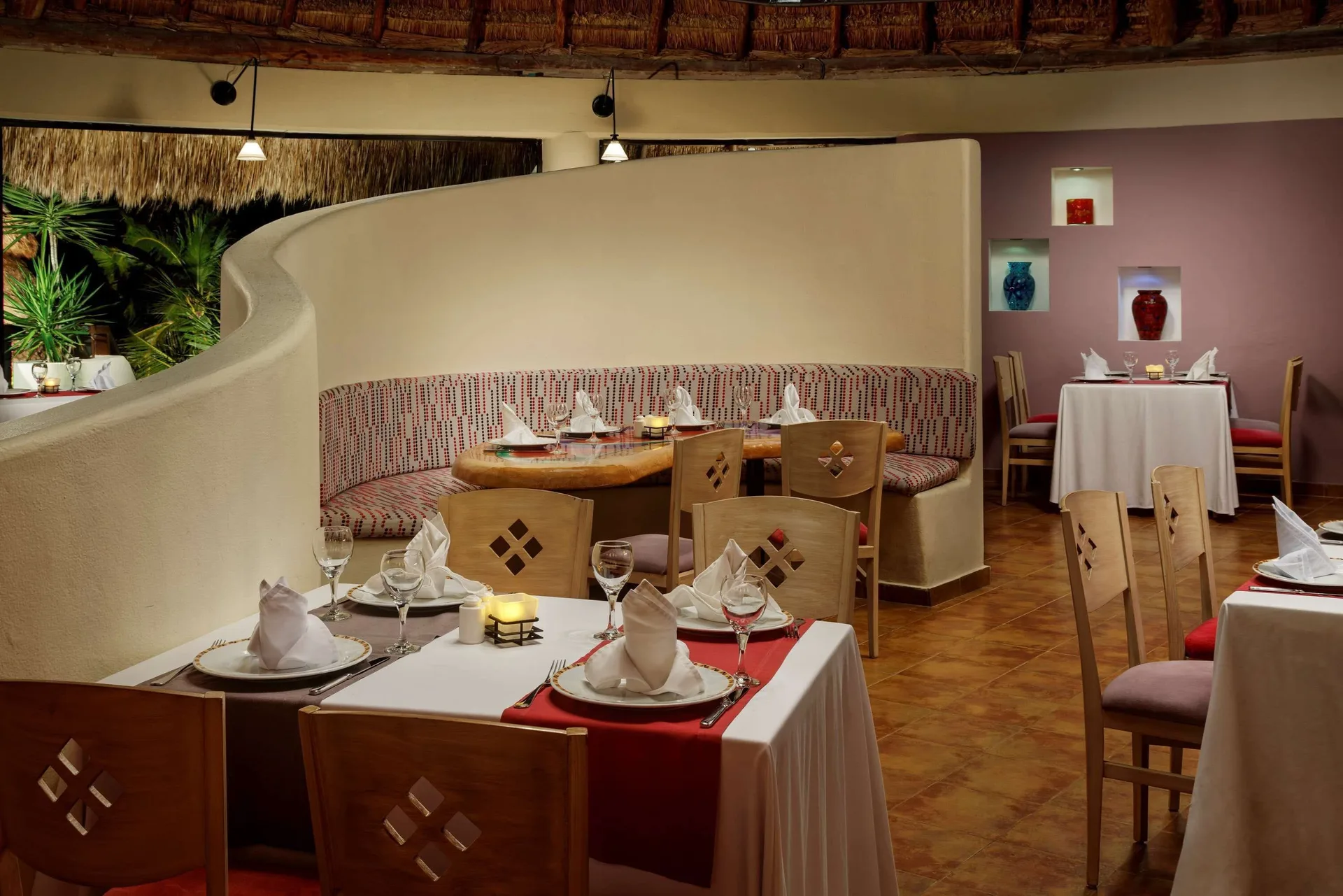 Restaurant tables with folded napkins and a curved booth at The Reef Coco Beach Resort & Spa.