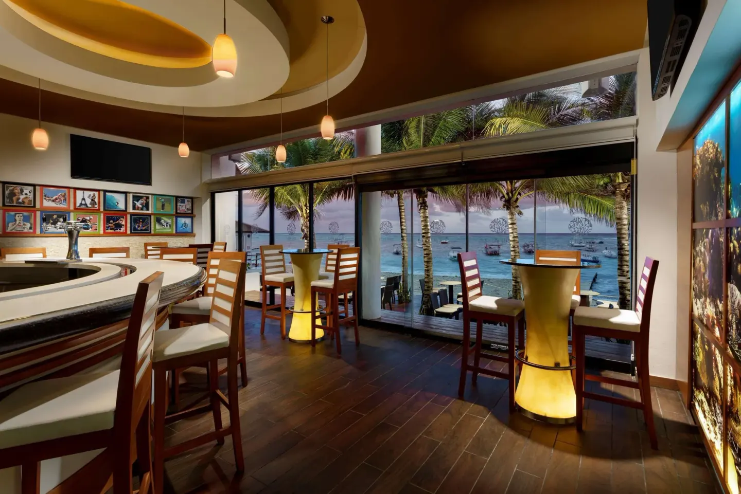 Ocean-view bar with high tables and sports photos at The Reef Coco Beach Resort & Spa.