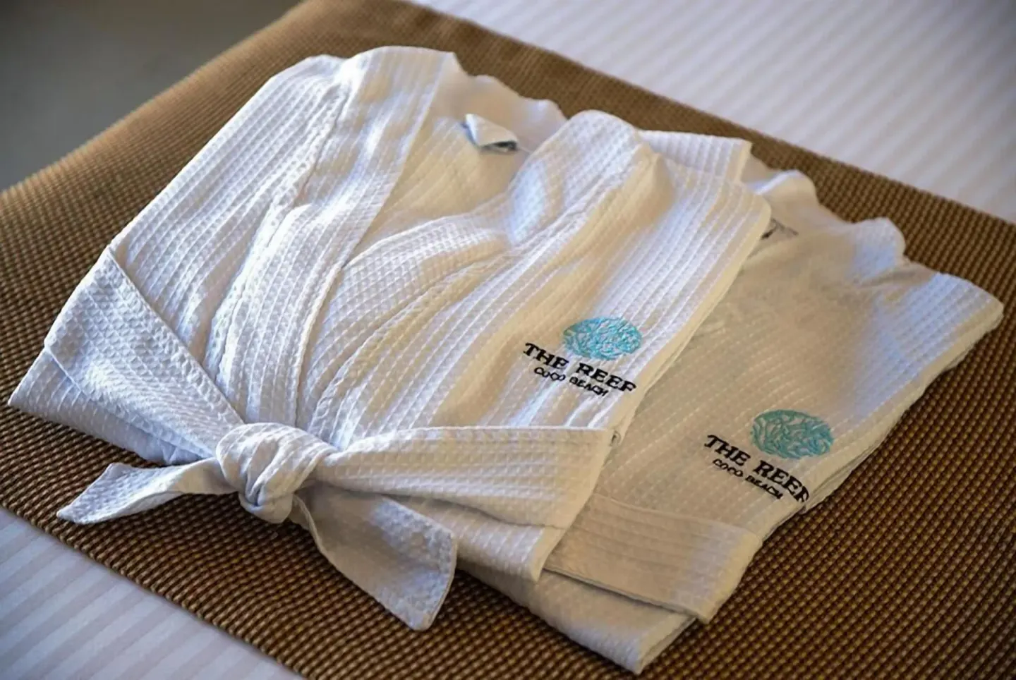 White robes laid on the bed in a Premium Partial Ocean View Room at The Reef Coco Beach Resort & Spa.