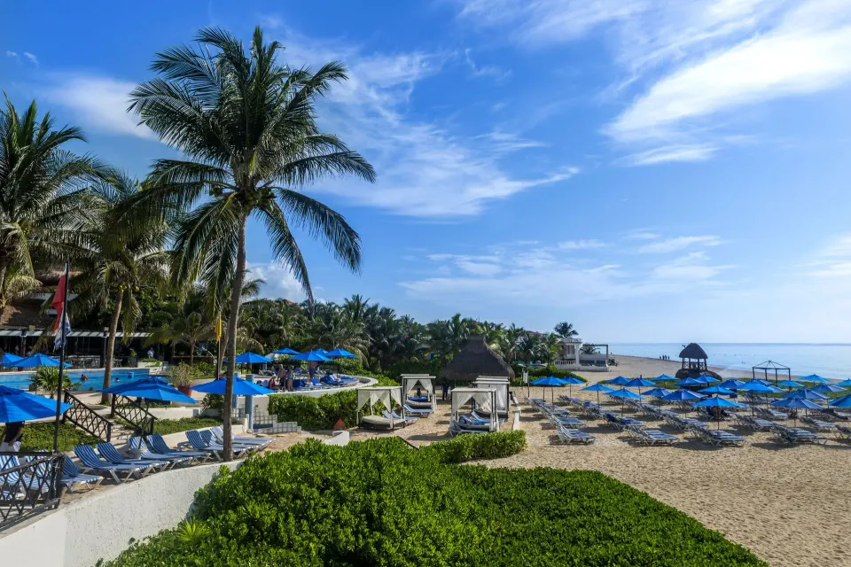 Sandy beach with blue umbrellas, sun loungers and palms at The Reef Playacar Beach Resort & Spa