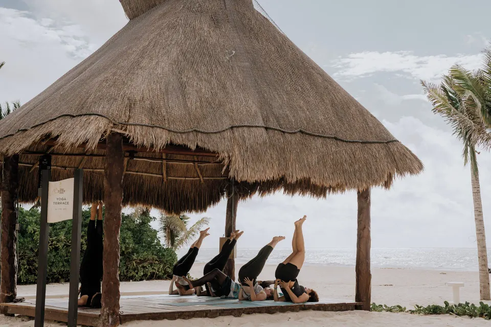 Group doing yoga under a thatched palapa on the beach at The Reef Playacar Beach Resort & Spa