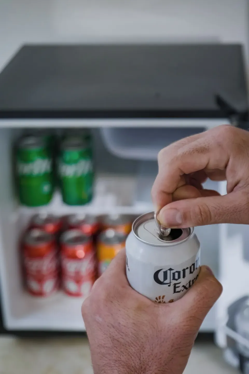 Guest opening a can of beer in front of a stocked minibar at The Reef Playacar Beach Resort & Spa