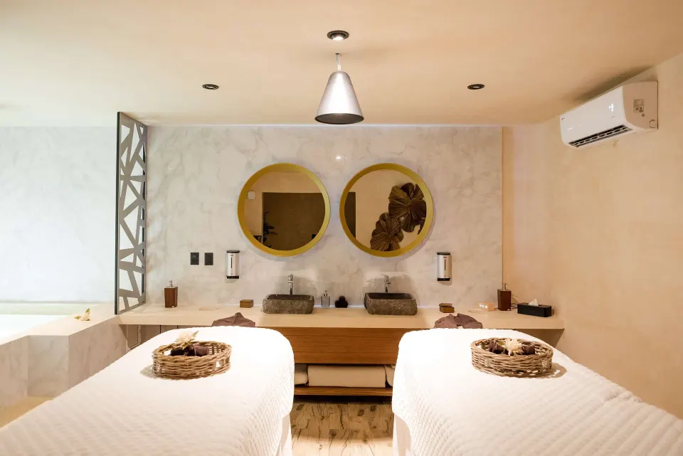 Twin massage tables and double-vanity sinks in a spa treatment room at The Reef Playacar Beach Resort & Spa