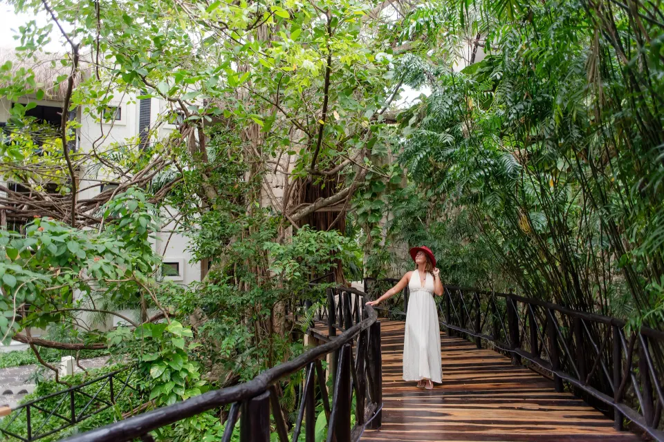 Woman walking on a wooden bridge through dense tropical foliage at The Reef Playacar Beach Resort & Spa