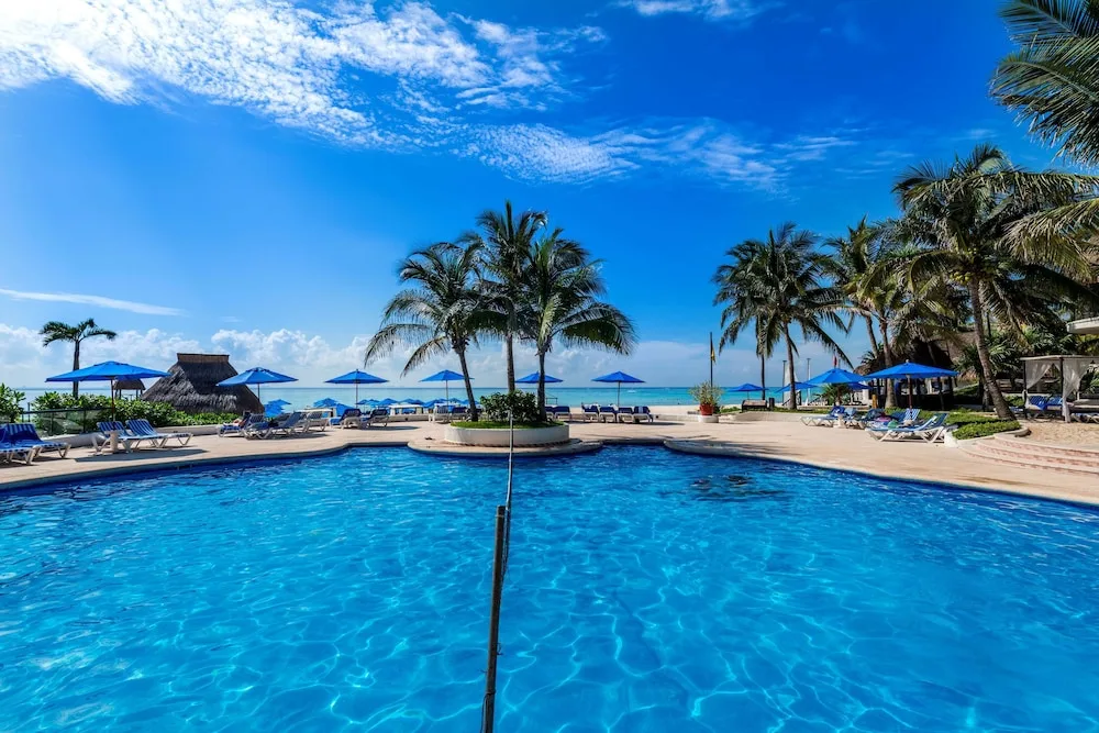 Wide pool view with palm trees and beach backdrop at The Reef Playacar Beach Resort & Spa